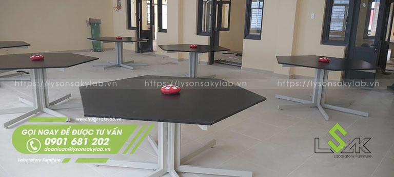 Bàn thí nghiệm vật lý hình lục giác khung sắt sơn tĩnh điện mặt bàn phenolic kháng hóa chất, trên bàn có gắn ổ điện